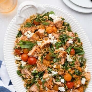 salmon and couscous salad on a white platter next to a blue and white striped napkin