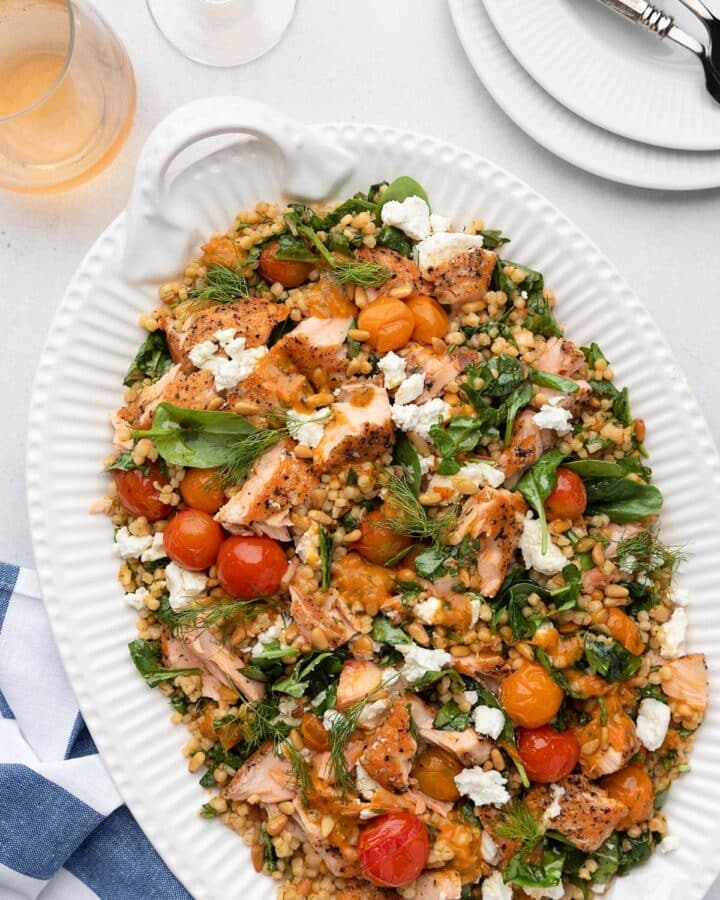 salmon and couscous salad on a white platter next to a blue and white striped napkin