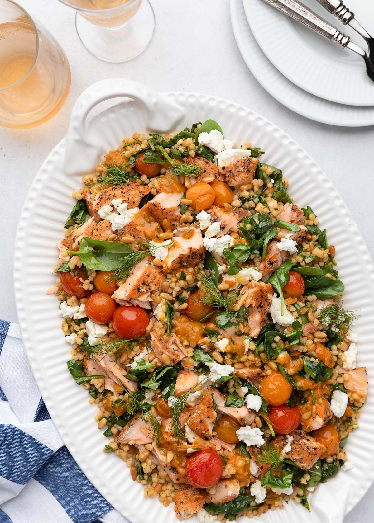 salmon and couscous salad on a white platter next to a blue and white striped napkin