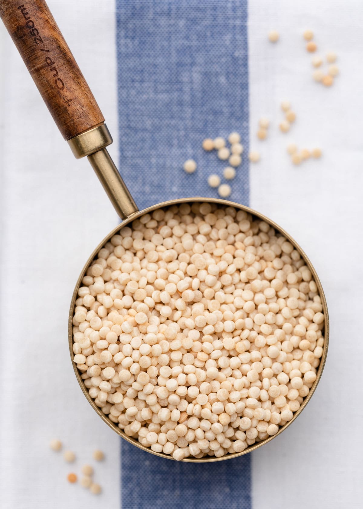 overhead of israeli couscous in a measuring cup on a blue and white striped napkin