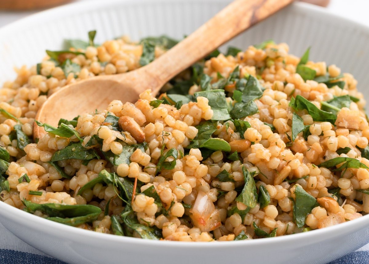 pearl couscous in a bowl with roasted tomato vinaigrette and chopped baby spinach leaves