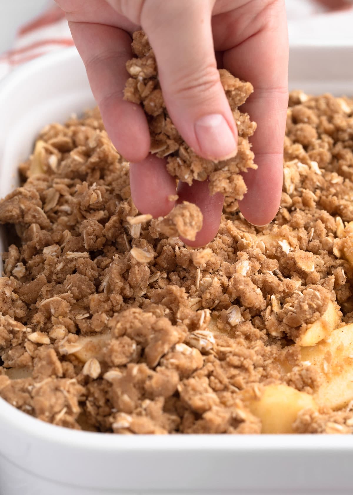 sprinkling crisp topping over sliced apples in a white baking dish