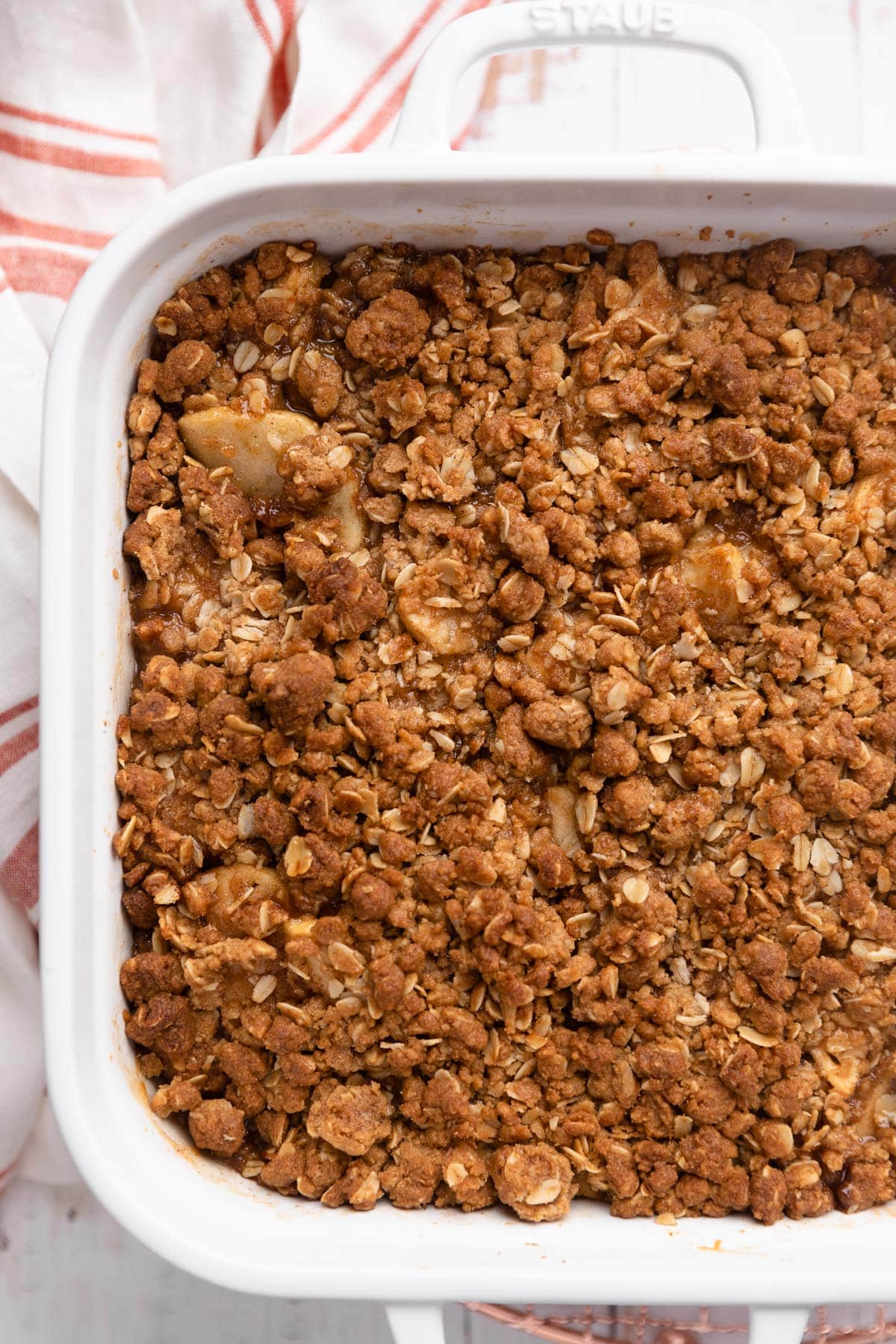 baked apple crisp in a white ceramic dish with a red striped napkin