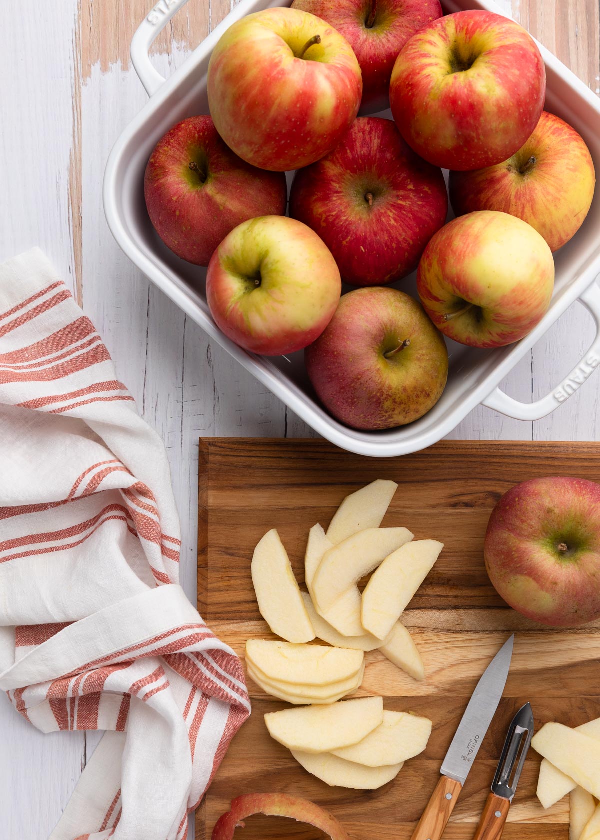 overhead photo of honeycrisp apples in a white baking dish, with sliced apples on a wood cutting board