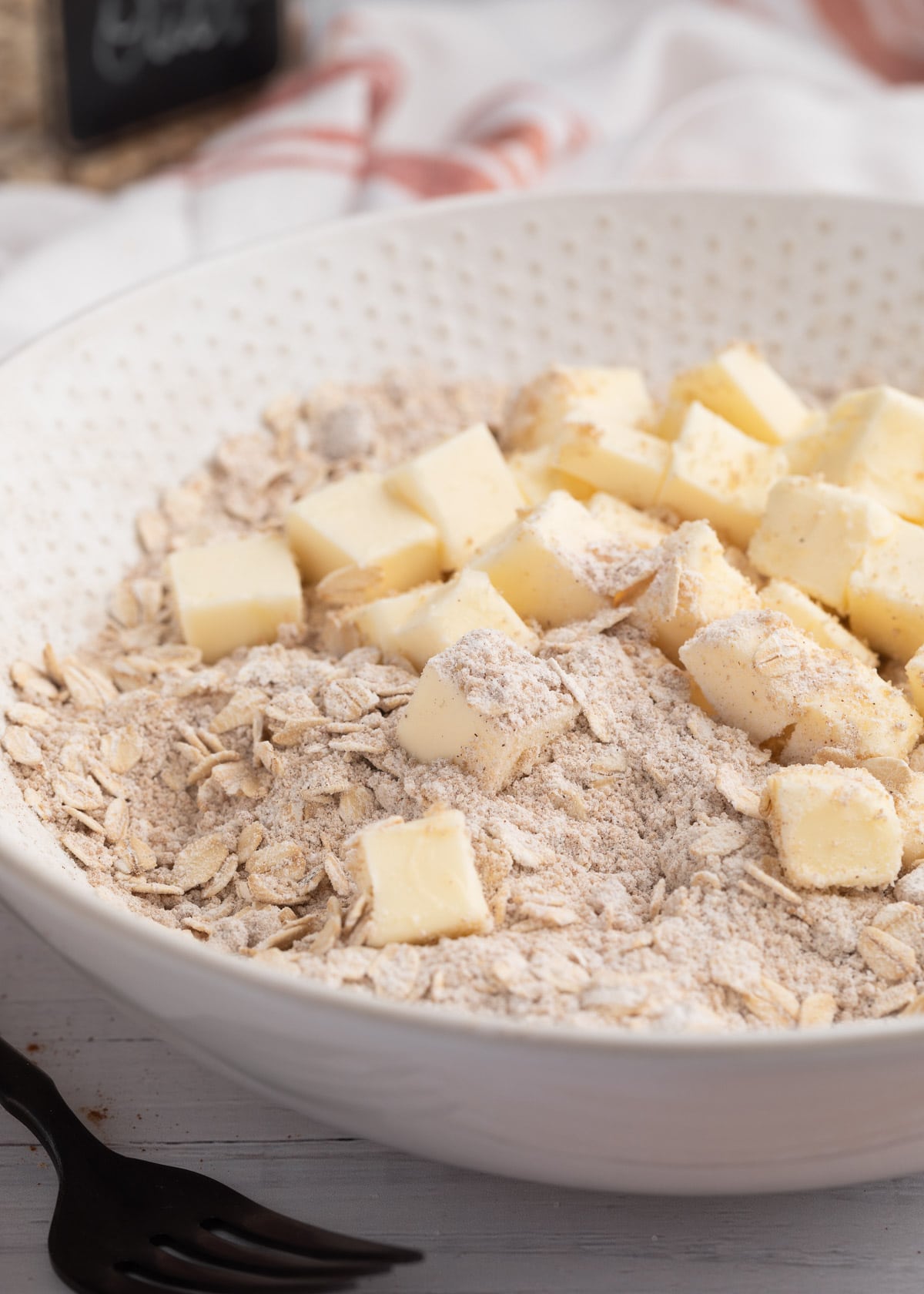 cubes of butter in a bowl of brown sugar, oats, and flour