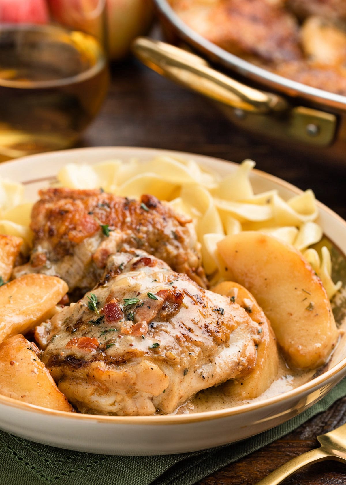 creamy chicken thighs with apples and hard cider sauce in a bowl with egg noodles