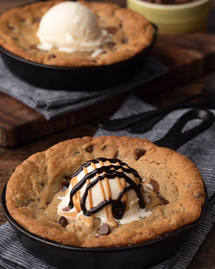 two peanut butter cookie skillets topped with vanilla ice cream; one with drizzles of peanut butter and chocolate sauces