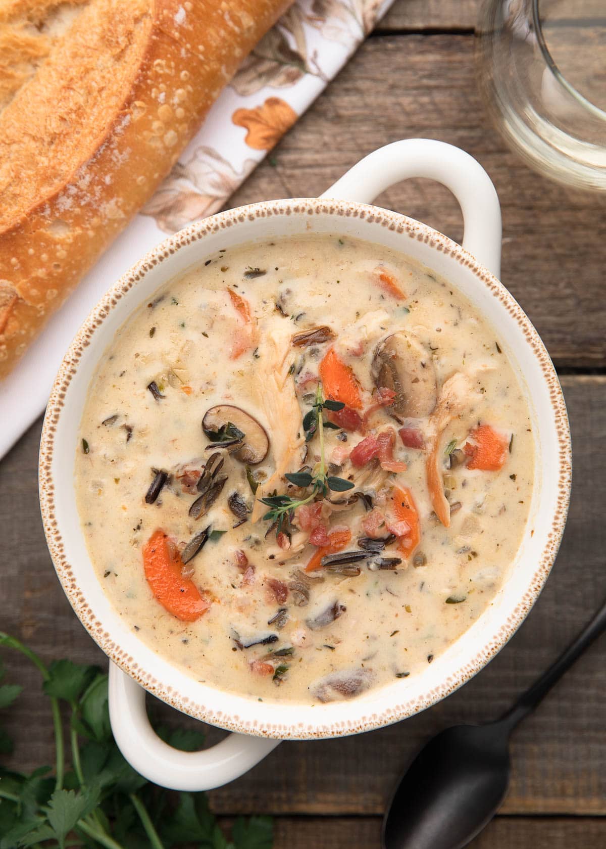 overhead photo of cream of turkey wild rice soup on a wood board next to a baguette