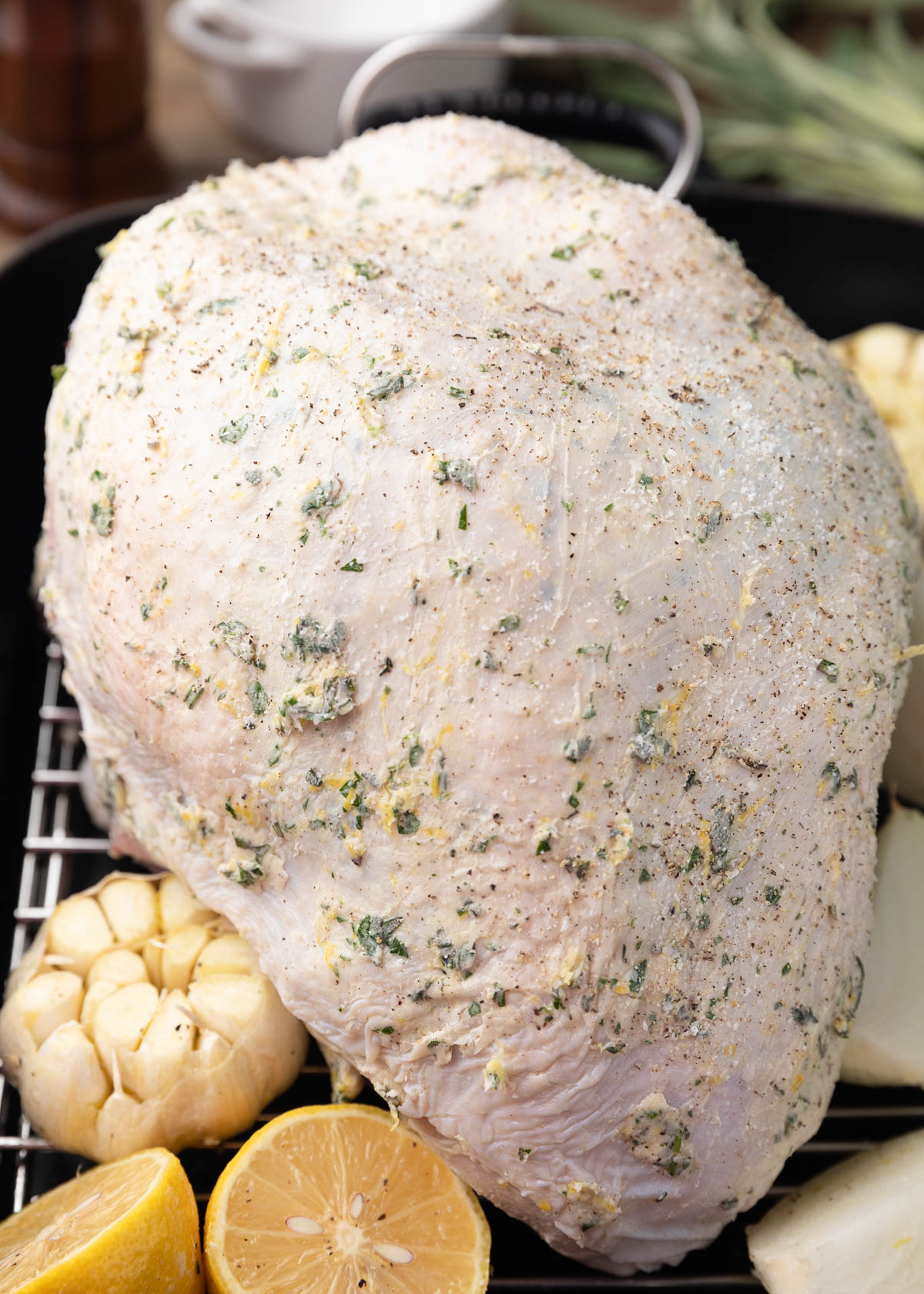 uncooked turkey breast in a roasting pan, covered with herb butter