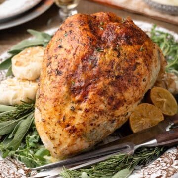 herb roasted turkey breast on a platter with fresh herbs and roasted garlic