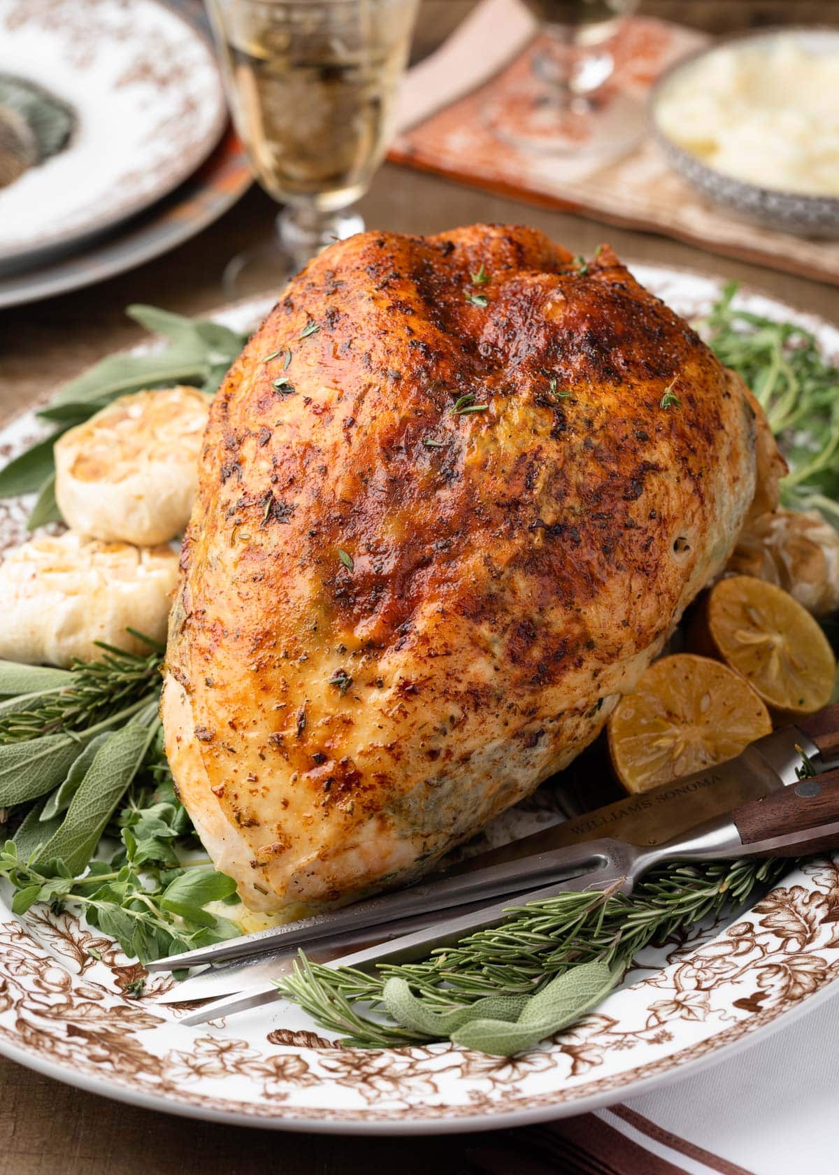 herb roasted turkey breast on a platter with fresh herbs and roasted garlic