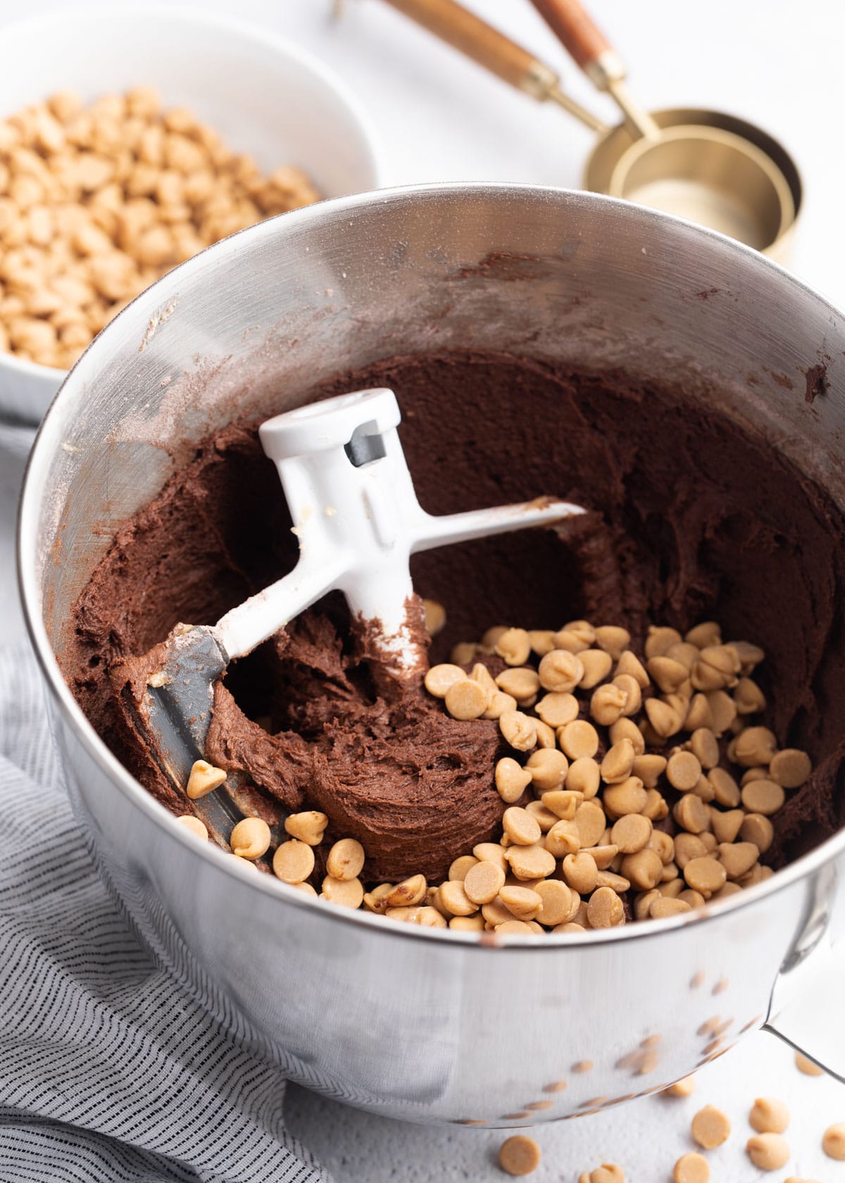 chocolate cookie dough in the bowl of a stand mixer with the paddle attachment and peanut butter chips