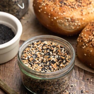 everything bagel seasoning in a glass jar, surrounded by everything bagels on a wood board