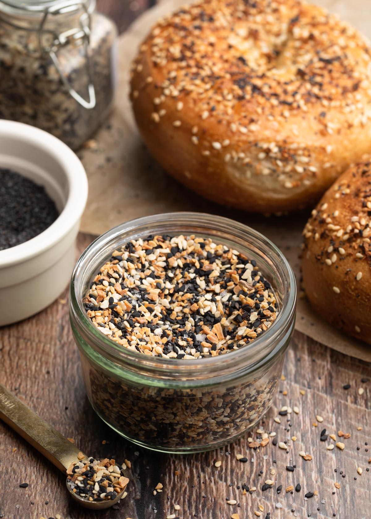 everything bagel seasoning in a glass jar, surrounded by everything bagels on a wood board