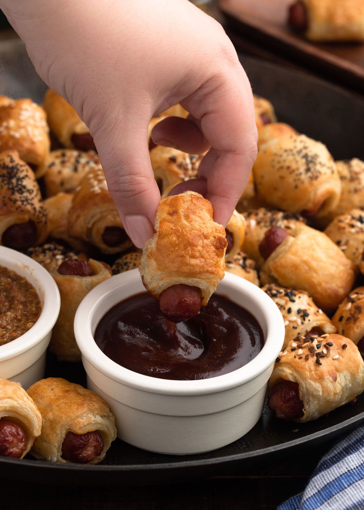 dipping a plain puff pastry pig in a blanket into barbecue sauce