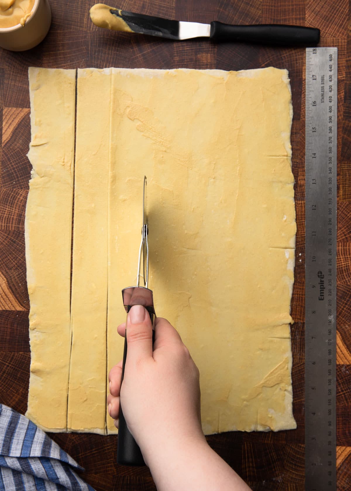 cutting strips of dijon-brushed puff pastry with a pizza wheel