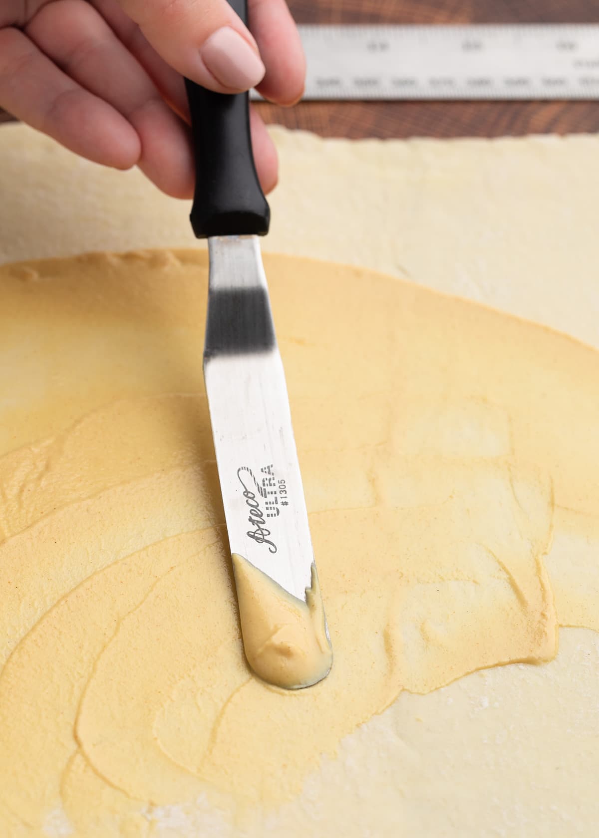 spreading Dijon mustard onto puff pastry with an offset spatula