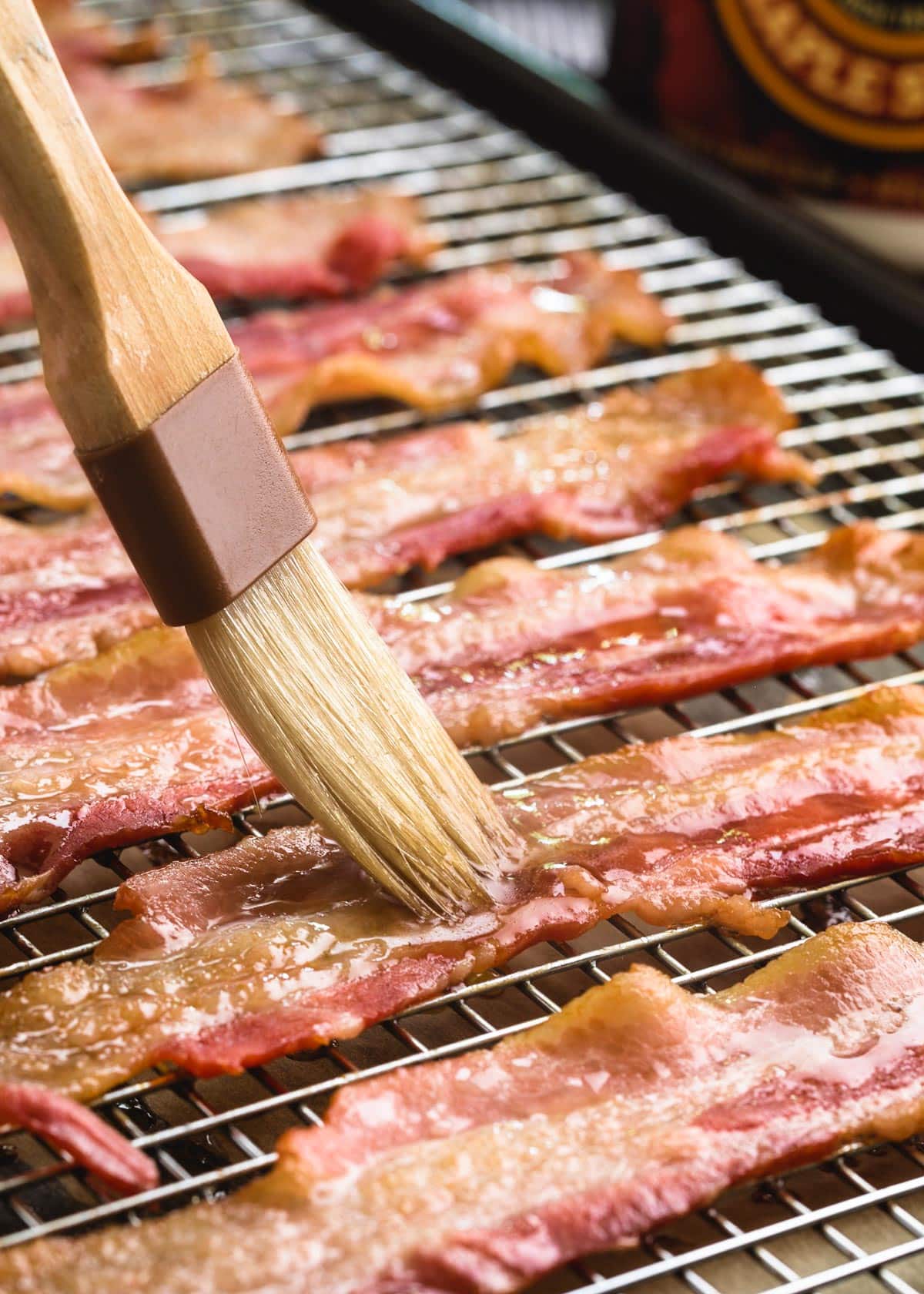 maple syrup being brushed onto partially-baked bacon strips on a wire rack