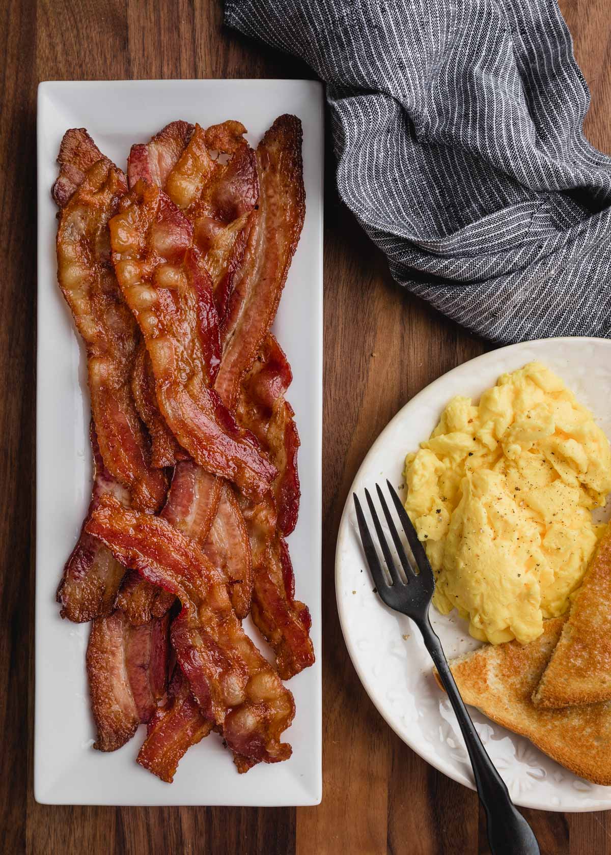 overhead di pancetta su un piatto rettangolare bianco con un piatto colazione di uova sul lato