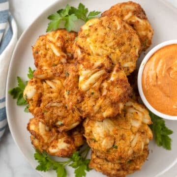 overhead photo of air fried crab cakes on a white plate with a bowl of remoulade