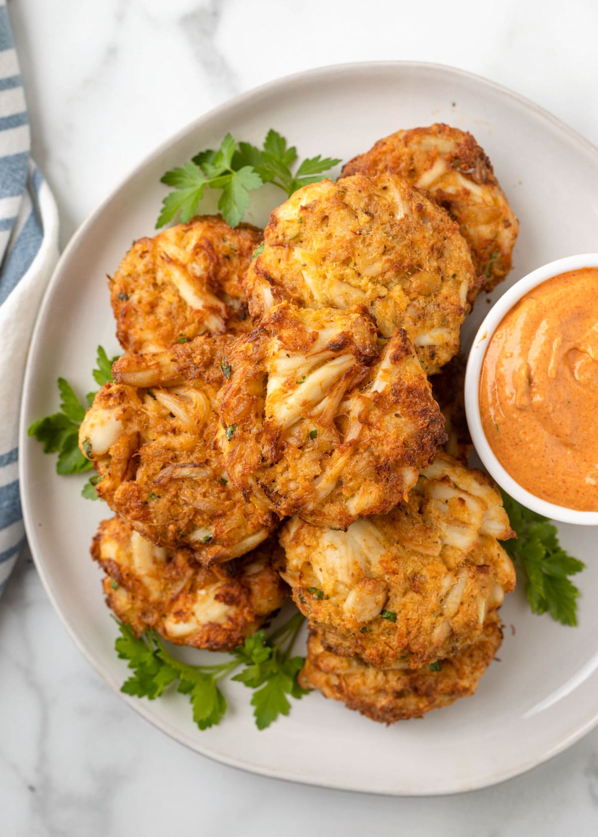 overhead photo of air fried crab cakes on a white plate with a bowl of remoulade