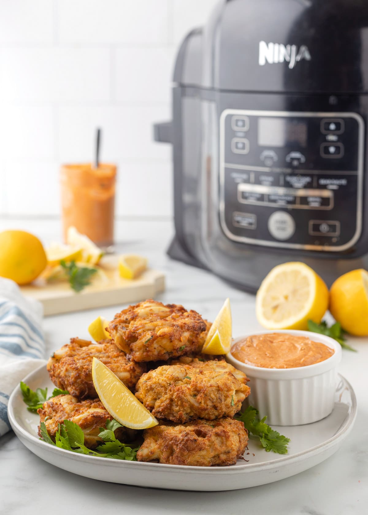 air fryer crab cakes on a white plate with lemon wedges and remoulade in front of a ninja foodi air fryer