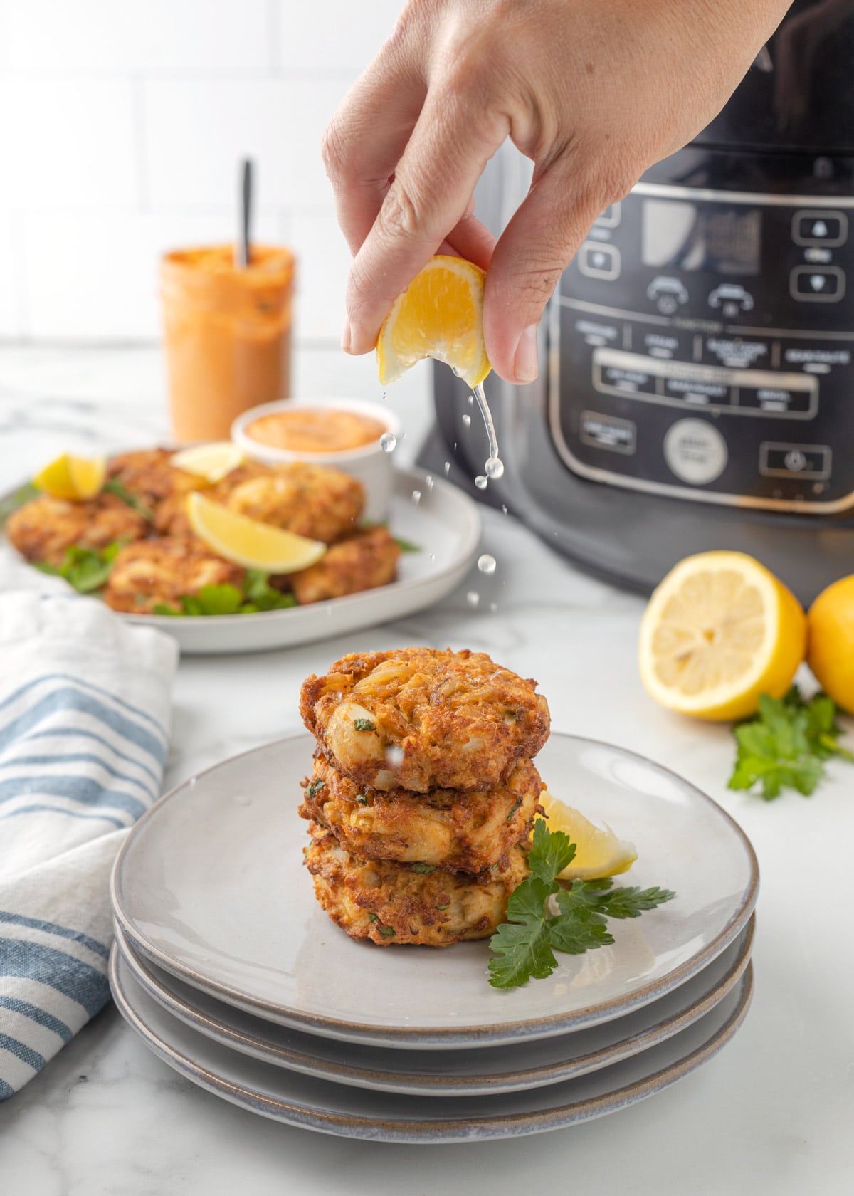 squeezing lemon over three crab cakes stacked on gray plates