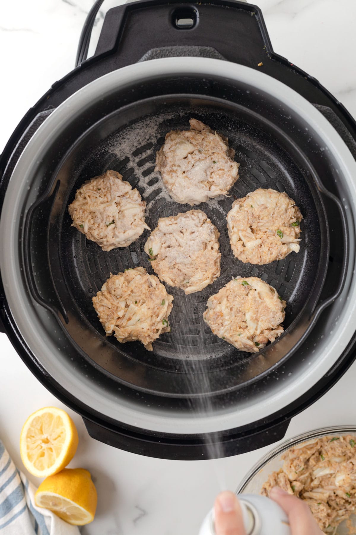 overhead view of spraying oil onto crab cakes in an air fryer basket