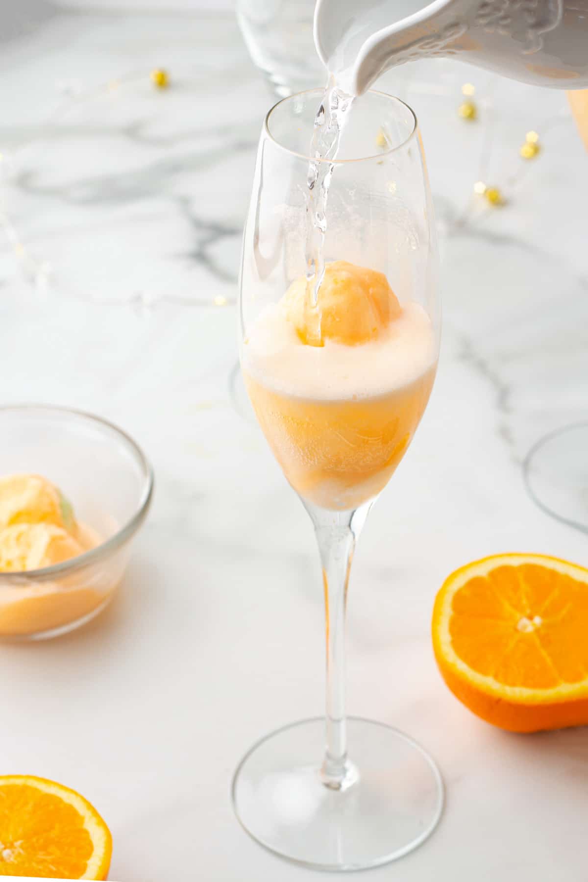 pouring sparkling water into a champagne flute with a scoop of orange sherbet