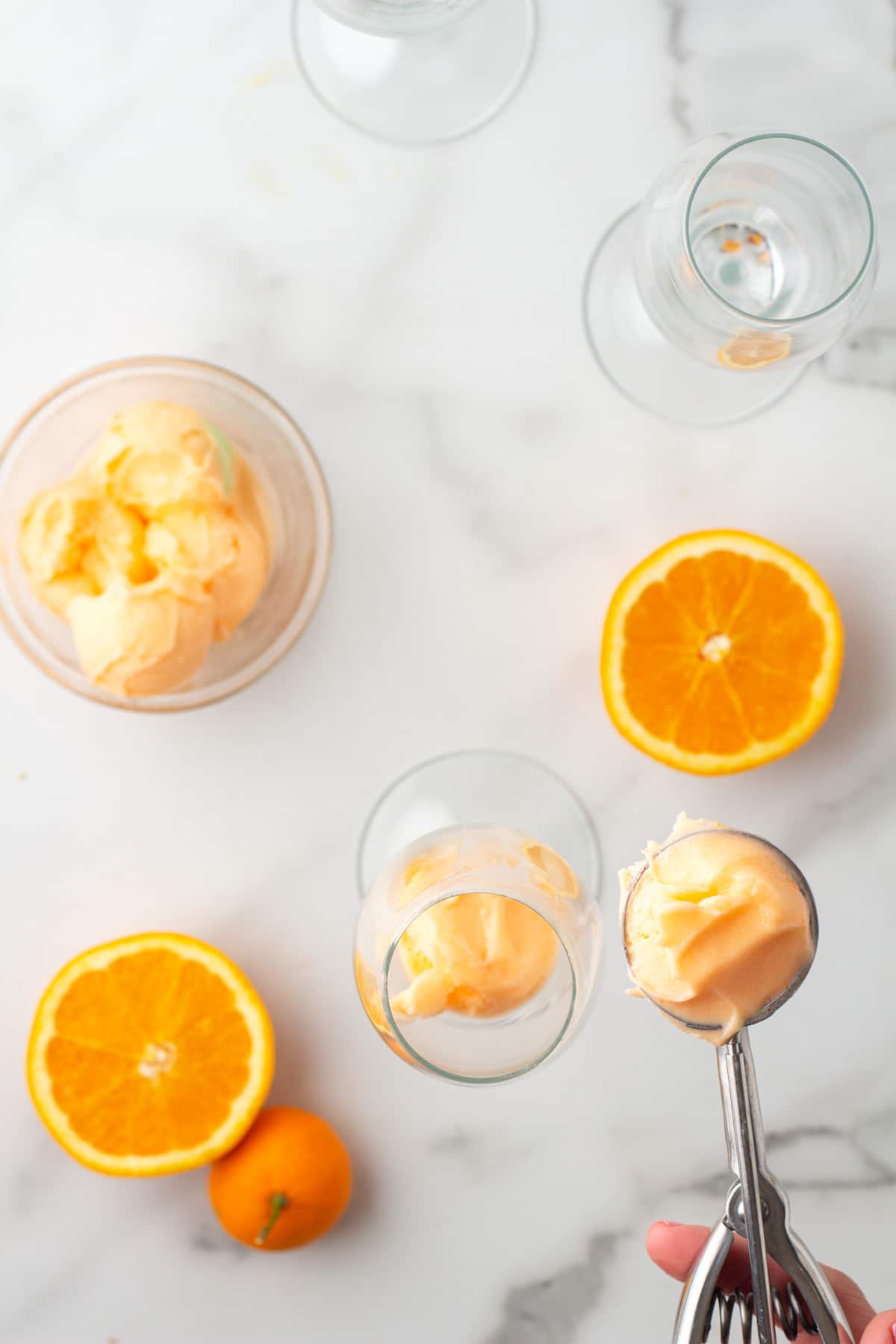 overhead view of scooping orange sherbet into a champagne glass with an ice cream scoop