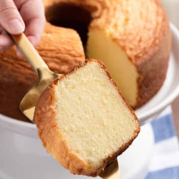 slice of vanilla pound cake on a gold cake server in front of a full pound cake on a white cake stand