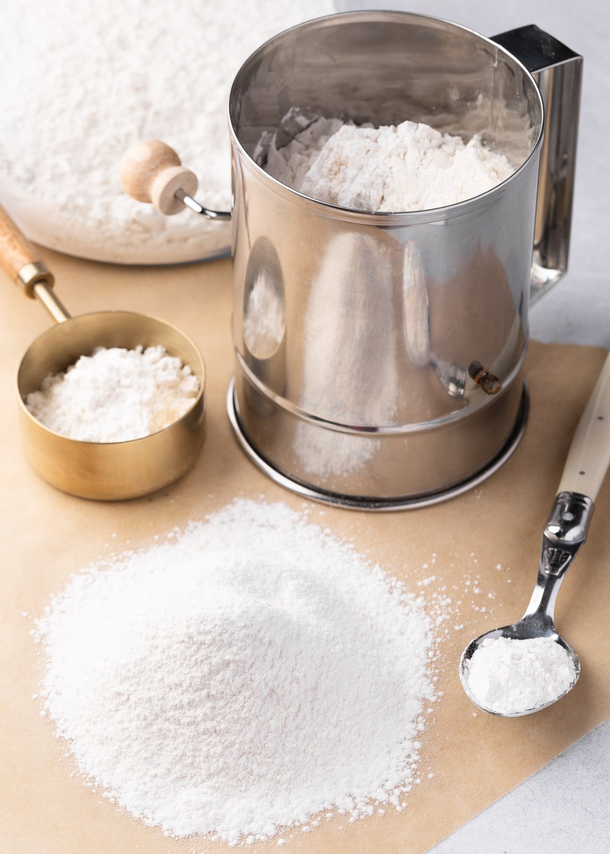 cake flour sifted onto a piece of parchment paper next to a stainless steel sifter