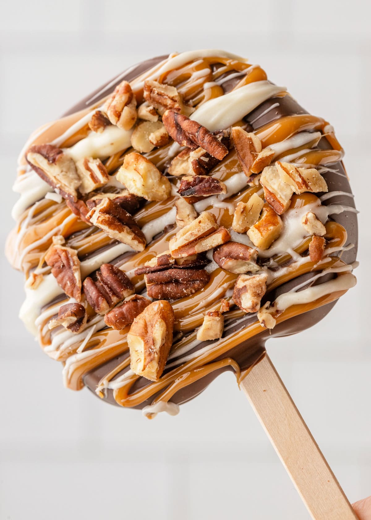 caramel apple slice on a popsicle stick with white chocolate drizzle and pecans