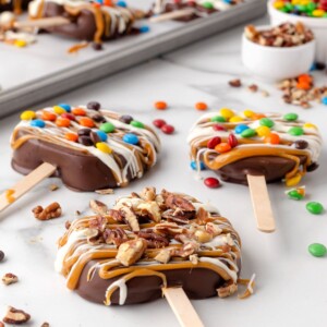 chocolate covered caramel apple slices decorated with candies and nuts on a white marble countertop