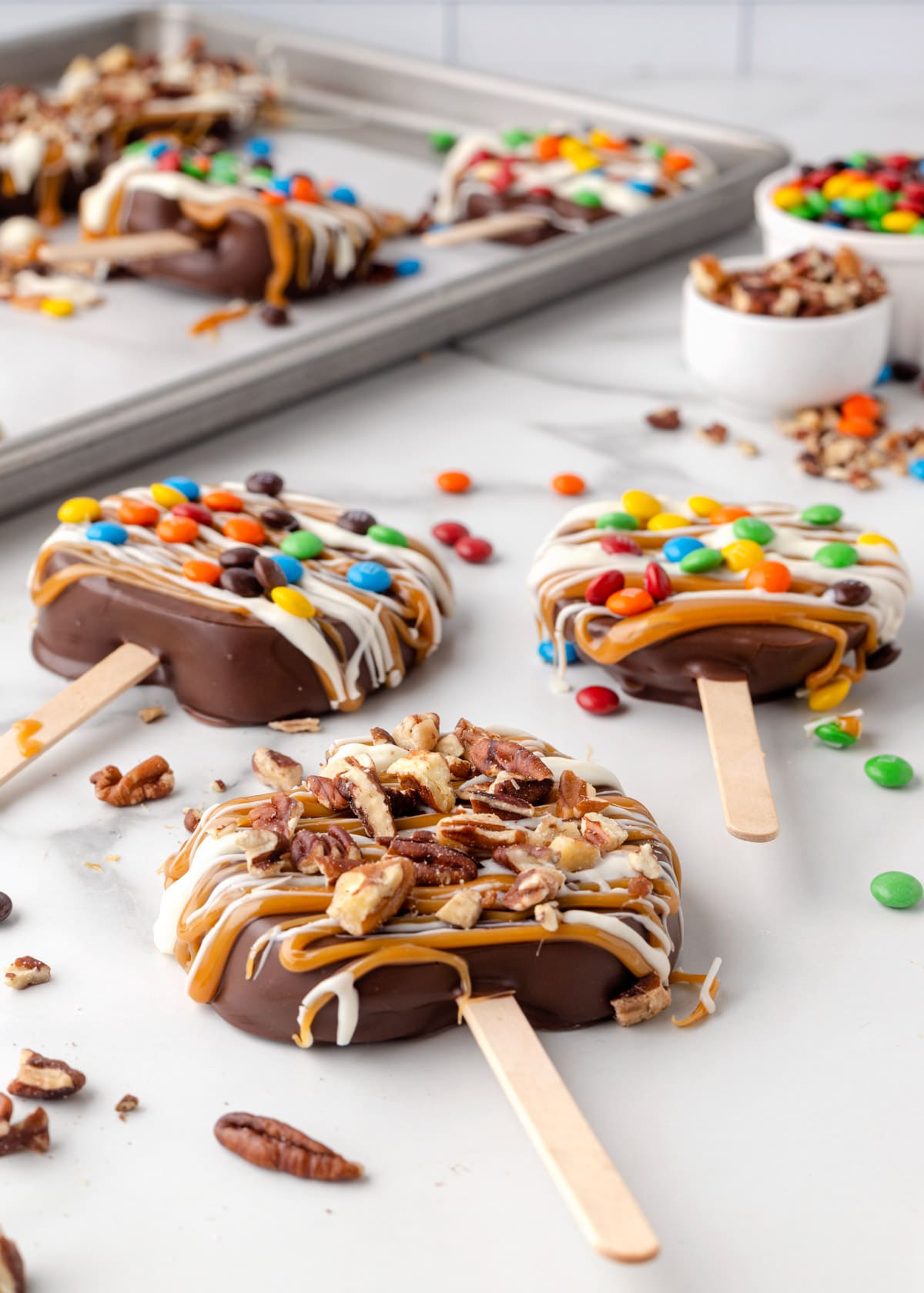 chocolate covered caramel apple slices decorated with candies and nuts on a white marble countertop