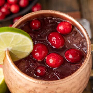 overhead of a cranberry moscow mule cocktail in a copper mug, garnished with fresh cranberries and a lime wedge