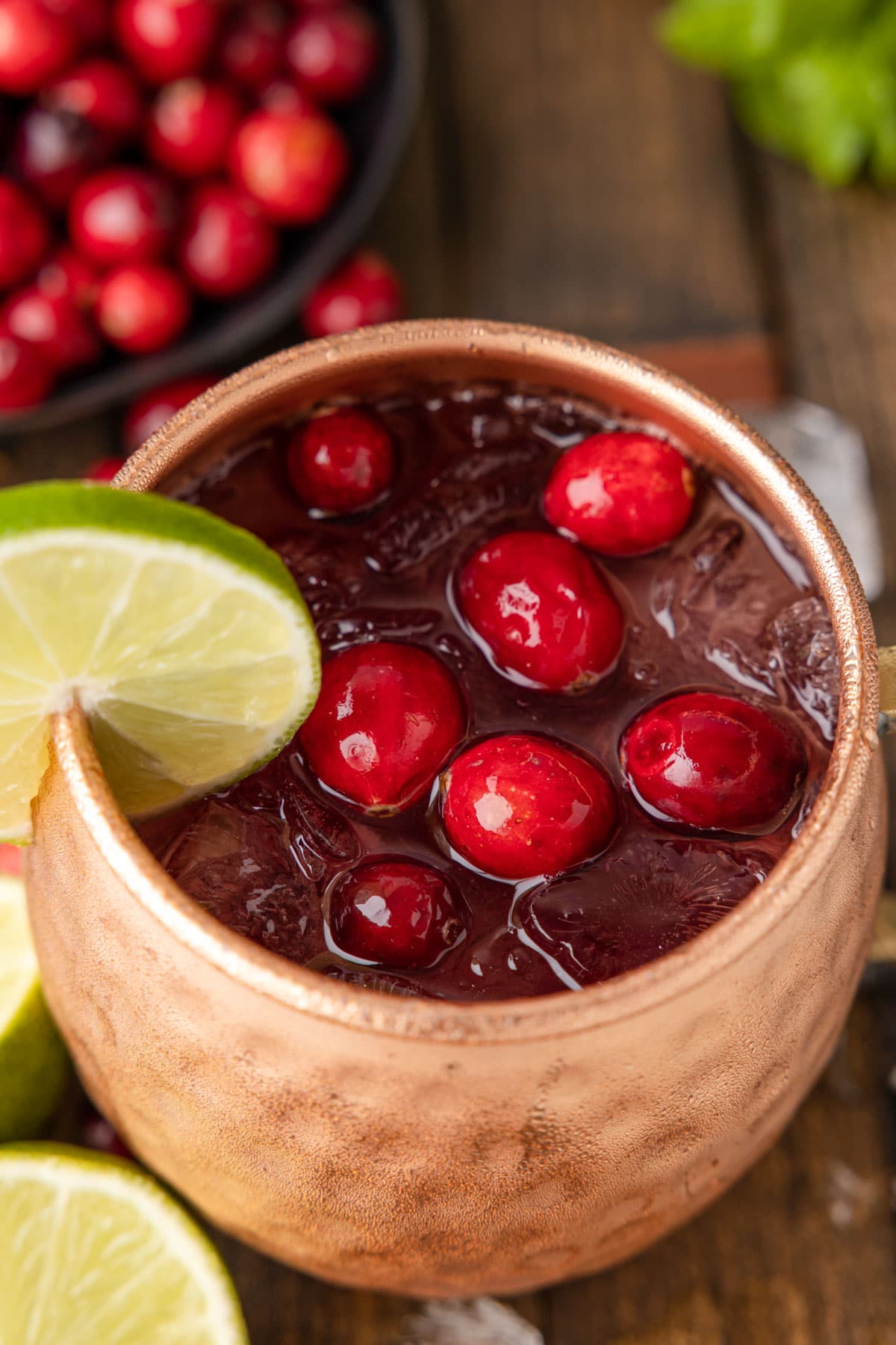 overhead of a cranberry moscow mule cocktail in a copper mug, garnished with fresh cranberries and a lime wedge