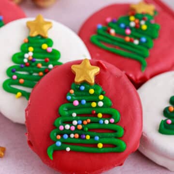red and white candy coated oreos with christmas tree decorations on a parchment-lined platter
