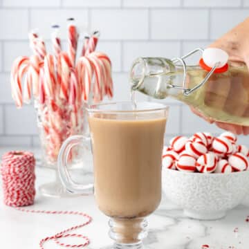 peppermint syrup being poured into a coffee drink in a glass mug