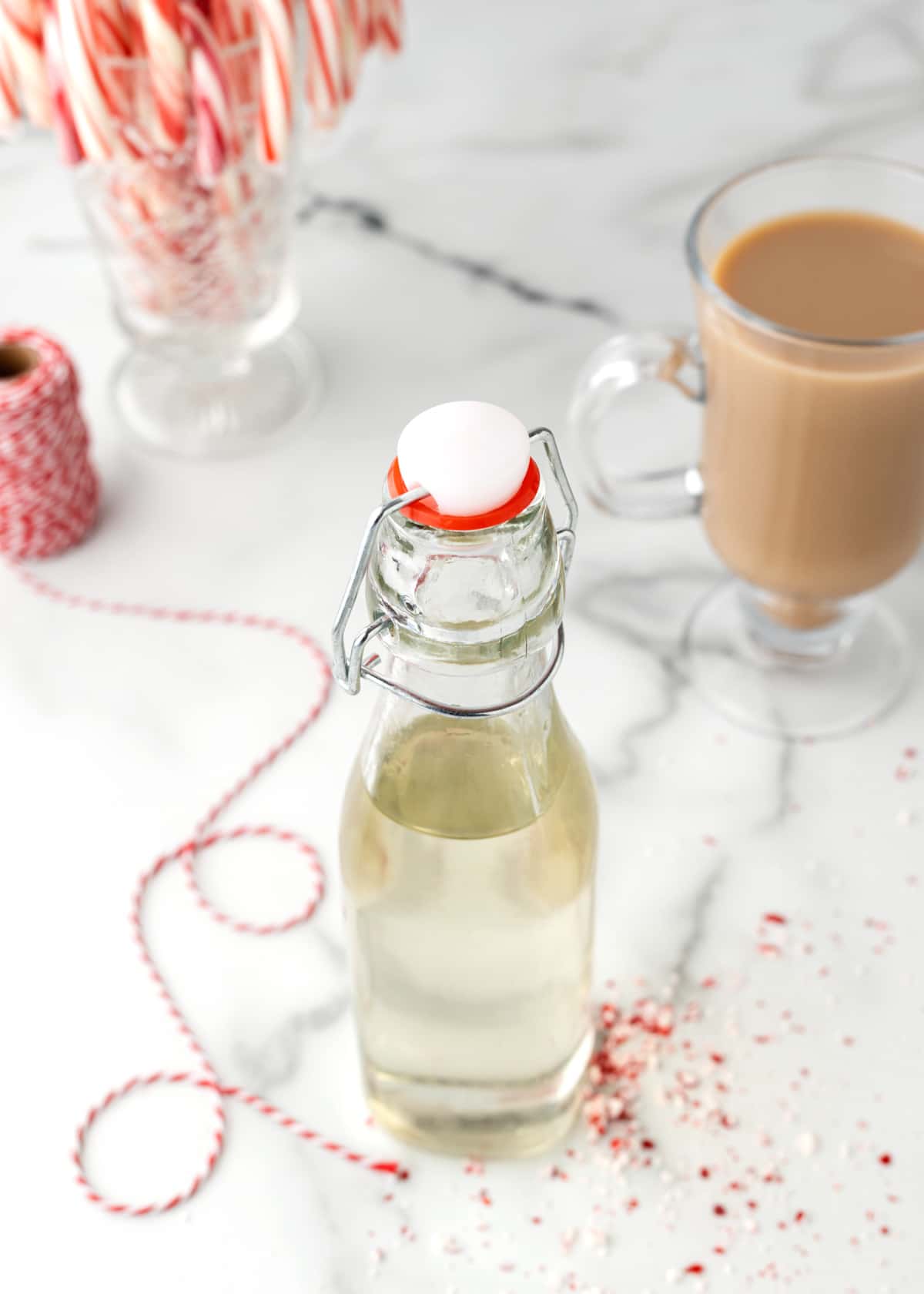 overhead photo of a bottle of peppermint syrup with a cup of coffee, candy canes, and red baker's string