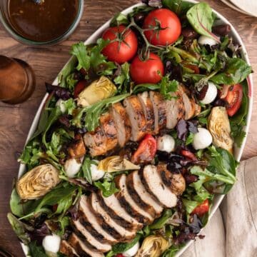 overhead photo of balsamic grilled chicken salad in a white over platter on a wood background