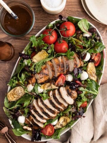 overhead photo of balsamic grilled chicken salad in a white over platter on a wood background