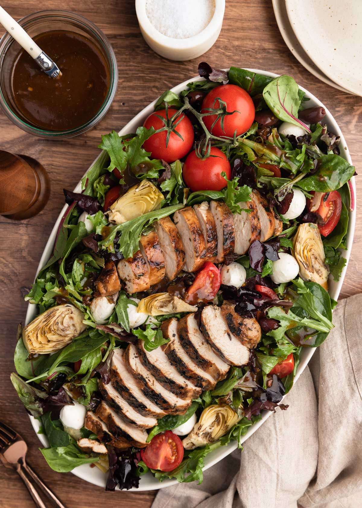 overhead photo of balsamic grilled chicken salad in a white over platter on a wood background