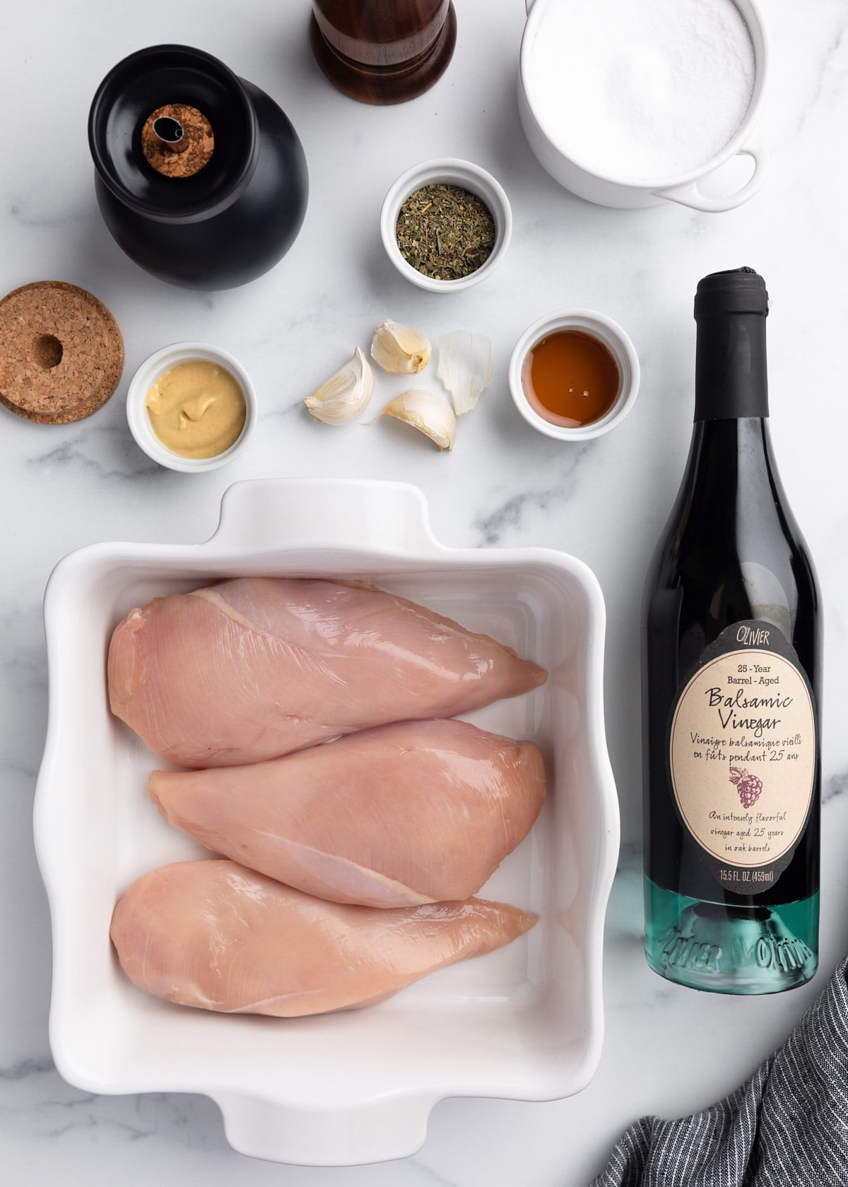 overhead photo of boneless skinless chicken breasts in a white baking dish, surrounded by a bottle of balsamic vinegar and marinade ingredients in small bowls