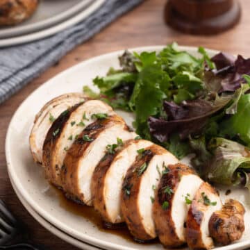 sliced balsamic marinated chicken breast on an ivory plate with a green salad