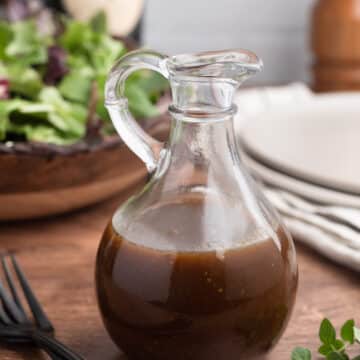 balsamic vinaigrette in a glass cruet in front of a bowl of spring mix lettuce