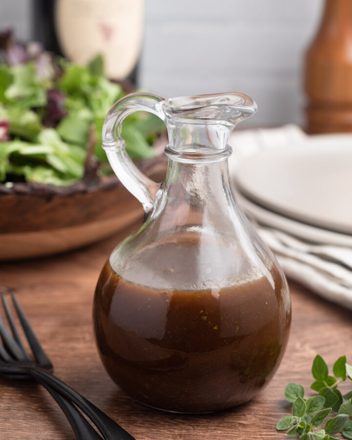 balsamic vinaigrette in a glass cruet in front of a bowl of spring mix lettuce