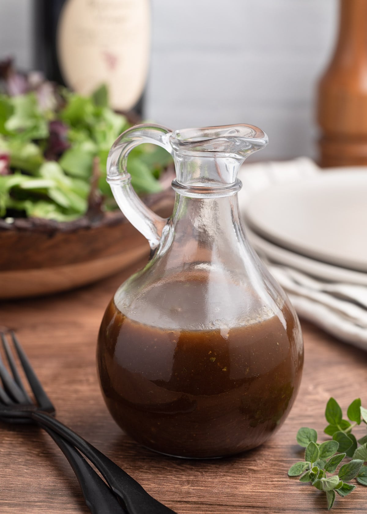 balsamic vinaigrette in a glass cruet in front of a bowl of spring mix lettuce