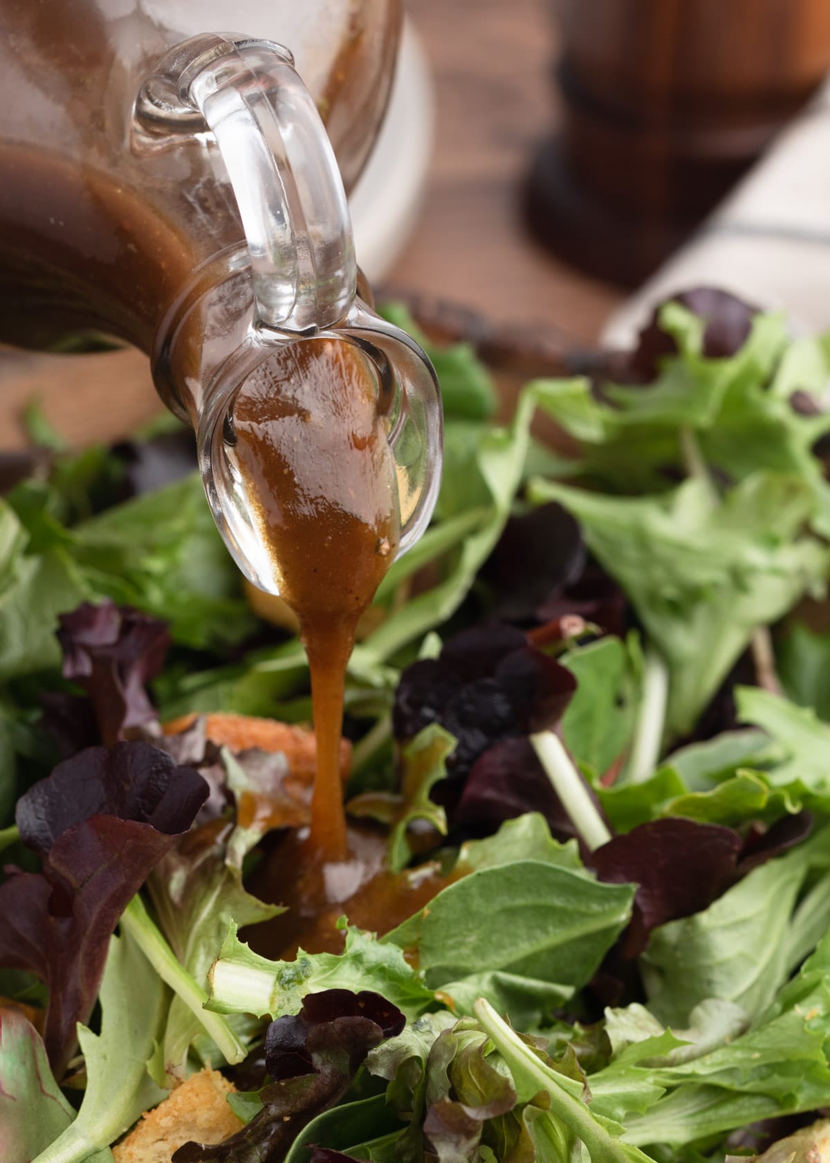 closeup of balsamic vinaigrette being poured from a glass cruet over spring mix greens