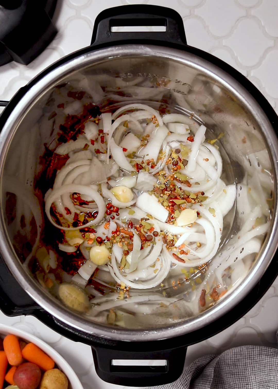 sliced onions, whole garlic cloves, and pickling spice in the bottom of an Instant Pot.